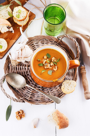 Bowl of creamy pumpkin soup with croutons, rustic bread, garlic and sage on white wooden background. Selective focusの写真素材