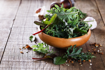 Leafy green mix of kale, spinach, baby beetroot leaves over rustic wooden backgroundの写真素材