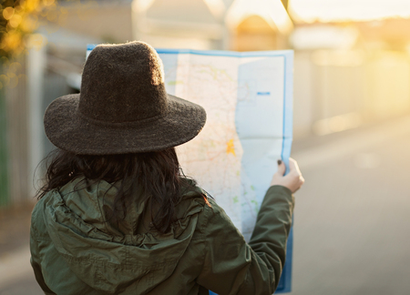 Travelling concept. Back view of a young girl in a khaki coat and hat looking at a map. Filters, color toning, selective focus, shallow depth of field, light leak, bokehの写真素材