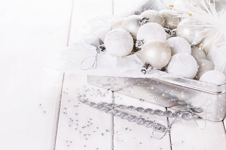 Retro style image of white and silver Christmas ornaments in a silver box over white wooden background. Selective focus, shallow DoFの写真素材