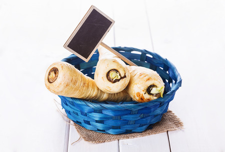 Parsnips in a blue woven basket and tag on white wooden background with copyspaceの写真素材