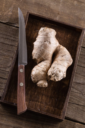 Fresh ginger root and knife over rustic wooden background