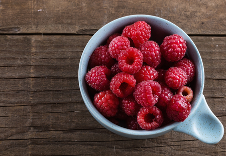 Top view of ripe fresh raspberries in bowl on wooden rustic background with copyspaceの写真素材