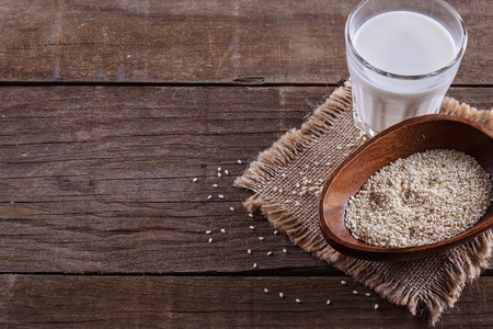 Glass of vegan milk and sesame seeds in a wooden bowl over rustic wooden background with copy spaceの写真素材