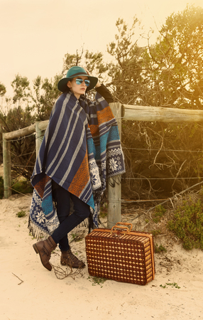 Young hipster girl in poncho with vintage suitcase at seashore. Instagram looking effect, filters, selective focus, color toningの写真素材