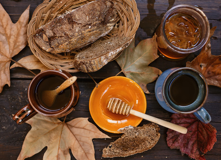 Instagram looking image with cups of tea, bread and honey over rustic wooden background with fall leaves. Selective focus, top viewの写真素材