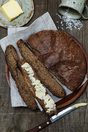 Top view image of artisan rye bread with butter and salt on a rustic wooden background close-upの写真素材