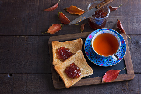 Cup of tea, two toasts, jar of jam and red leaves over rustic wooden background. Top viewの写真素材