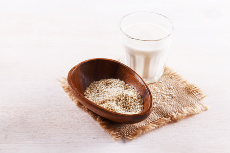 Glass of sesame seed milk and seeds in a wooden bowl over white wooden backgroundの写真素材
