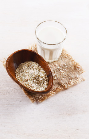Glass of sesame seed milk and seeds in a wooden bowl over white wooden backgroundの写真素材