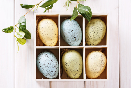 Easter decor eggs in a wooden box over white wooden background with copy spaceの写真素材
