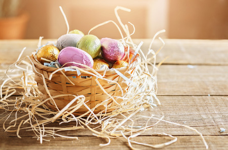 Vintage looking image of Easter eggs in a woven basket over wooden background. Color toning, retro effect filtersの写真素材