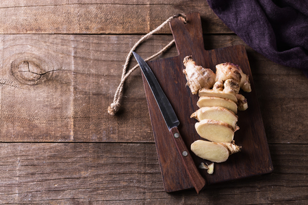 Top view image of fresh ginger root cut on the pieces and knife on a cutting board over rustic wooden backgroundの写真素材