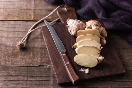 Fresh ginger root cut on the pieces and knife on a cutting board over rustic wooden backgroundの写真素材