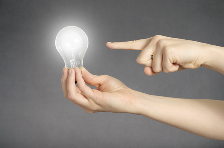 A finger pointing to a glowing light bulb in a handの写真素材