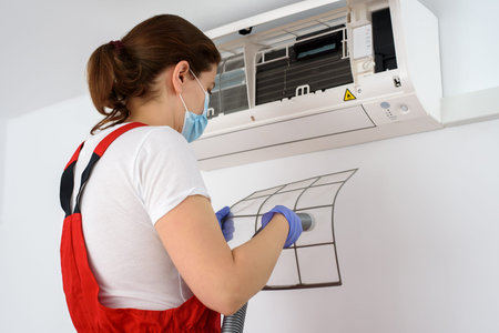Female technician wearing face mask and cleaning air conditioner