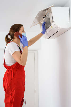 Female technician using smartphone and repairing air conditionerの写真素材