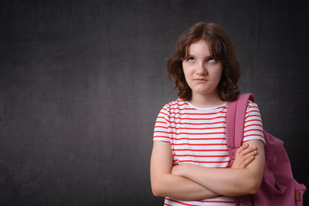 Bored schoolgirl holding backpack, looking at camera