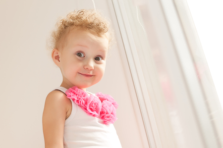 Funny little girl with curly hair looking at the photographer. The girl curled a face funny. Portrait of a beautiful child close-up.の写真素材