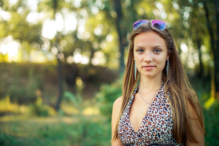 Beautiful girl in light sarafan with developing hair on forest background. Girl is smiling standing in background of setting sun.の写真素材