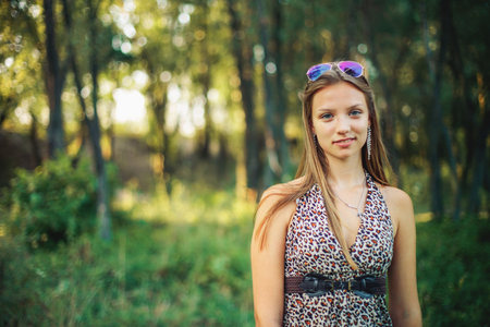 Beautiful girl in light sarafan with developing hair on forest background. Girl is smiling standing in background of setting sun.の写真素材
