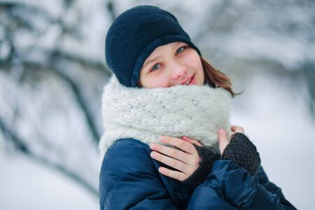A young girl in a long white scarf of snow-covered branches of trees in the city.
