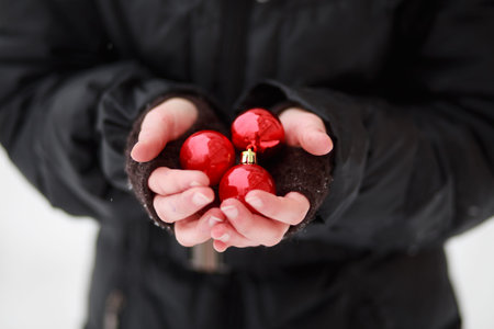 The frozen palm of a child standing in the cold and holding three red balls to decorate a Christmas treeの写真素材