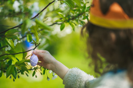A girl in a crown hangs a Easter egg on a branch. Preparation for Easter. Hidden on a blossoming...