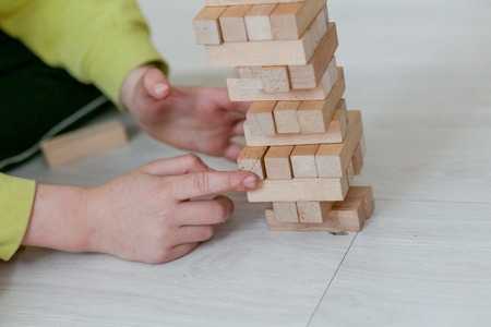 The child plays in a tower of wooden bars. Floors of wooden pieces. The child takes out the bars from the floors of the tower. Board game.の写真素材