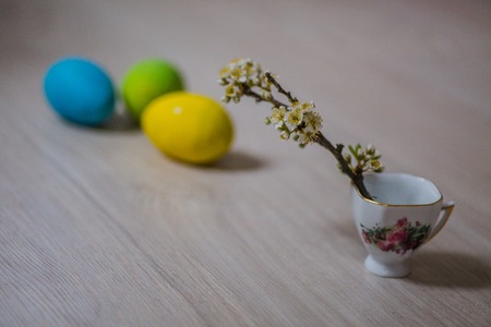 Three Easter eggs near a cup with a sprig of plum. Easter background for mobile and computer screens. Copy spaceの写真素材