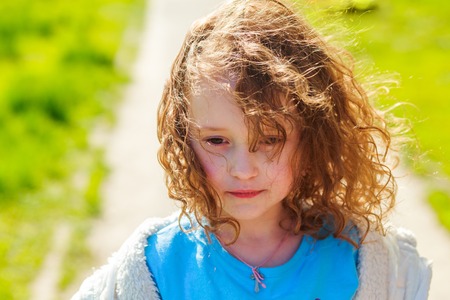 Beautiful curly girl on a background of green grass. Pensive child with sun in hair.の写真素材