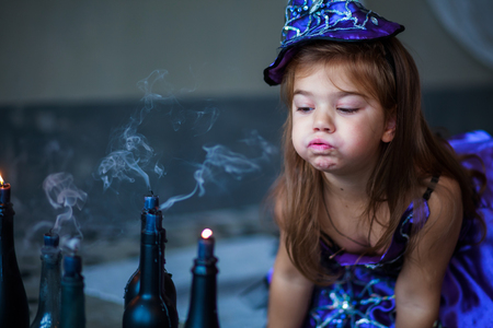 girl in the witch costume frightens. child is celebrating Halloween. Little girl blowing out candles on Halloween.の写真素材