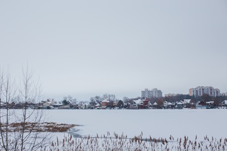 Ellings near frozen river against the backdrop of the town of Ukrainka. Dry reeds by the water. Winter landscape. Copy spaceの写真素材