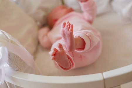 A newborn baby is lying in a white round bed, on a white sheet, with white cushion ribs. The child raised his bare feet and spread his fingers.の写真素材
