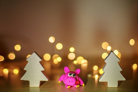 The symbol of the year 2019 pig of plasticine. Christmas background. Pig at the Christmas spruce. Bokeh for new year greeting card.の写真素材