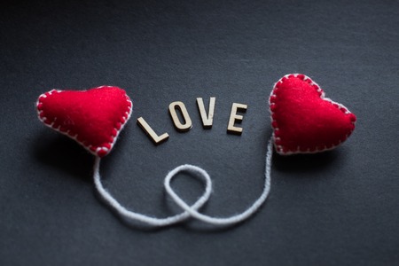 Happy Valentines Day romantic greeting card. Two red heard from felt. Handmade heart on black background. Text Love. Place for text, copy space.の写真素材