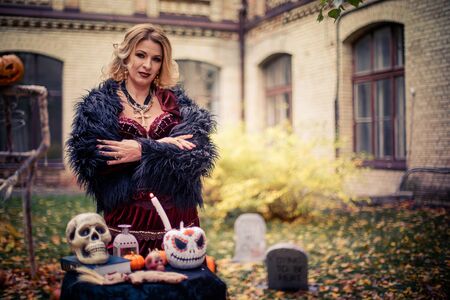 woman in witch's costume is conjuring. Table of sorceress with skulls and pumpkin decorated for the day of dead. Halloween celebration in costume.の写真素材