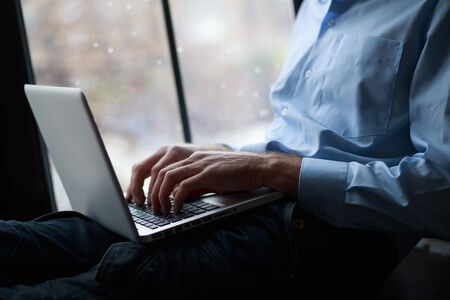 Hands of successful businessman freelancer writing message on laptop keyboard. Freelancer working sitting on windowsill next to brick wall. Online business conceptの写真素材