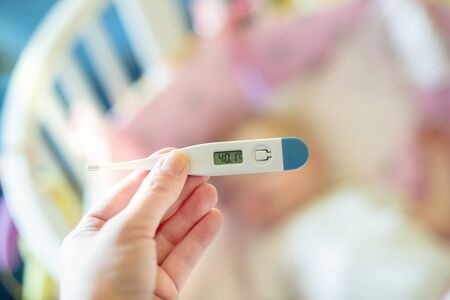 Close-up medical thermometer, Parent measuring temperature of ill kid, 1 years old toddler girl gets high fever lying on bed. fever in child.の写真素材