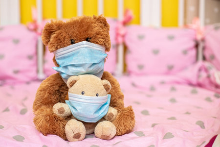 large teddy bear in protective mask and small teddy bear in medical mask sit in cot. Sick animals during epidemic. Coronovirus, quarantine, pandemic, flu, cold,illness. Medicine concept and health.の写真素材