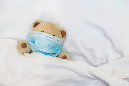 small toy bear lies in bed. Toy in protective medical mask in children's games. Coronovirus,...