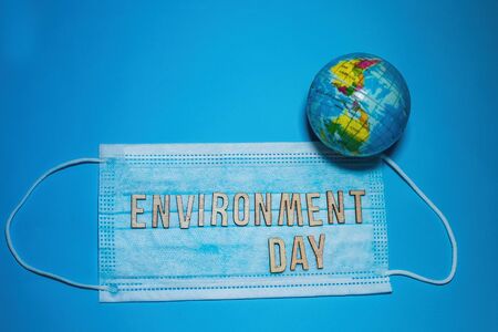 Word ENVIRONMENT DAY of wooden letters against background of protective medical mask. globe model Earth on blue background. Environmental protection concept.の写真素材