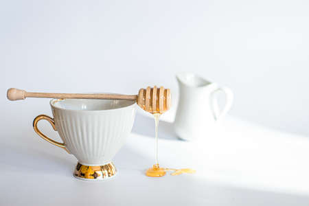 White cup with stick for honey Fresh honey flowing on table with wooden honeysbast.の写真素材