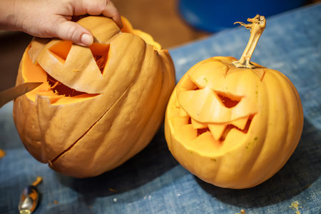 halloween, decoration and holidays concept - close up of woman with knife carving pumpkin or jack-o-lantern at home