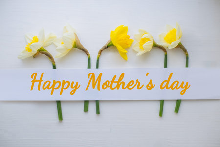 HAPPY MOTHERS DAY wording on white wood Creative layout made with narcissus flowers. Flat lay. Narrow Paper Strip for copy space. Top view. Easter, 8 march, mothers day, spring backgroundの写真素材