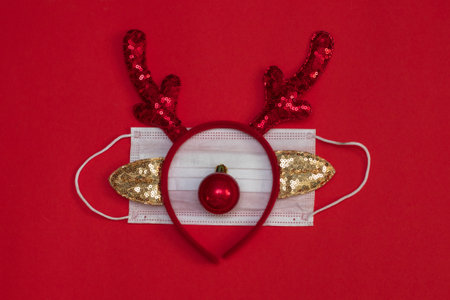 Medical face mask with deer antlers on red background. concept of christmas in face of COVID-19 pandemic.の写真素材