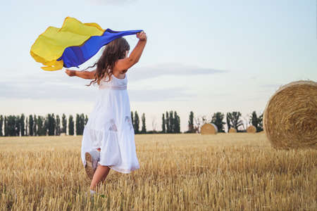 large flag of Ukraine in hands of child on Independence Day. Happy Ukrainian girl runs on a wheat field. Flag Day. Constitution dayの写真素材