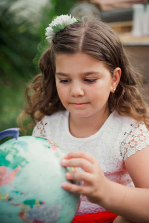 cute schoolgirl girl explorer looking at globe by pointing finger at it in the park. Adventure, dreaming about travel life concept. Studying geography at schoolの写真素材