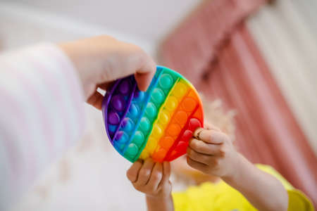 mother plays with young daughter. Womens hand holding popping  toy. girl takes fashionable toy from momの写真素材