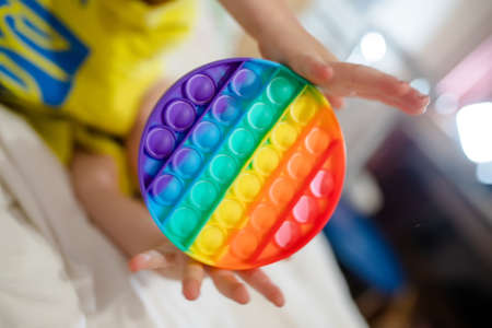 hands of toddler child are holding round popping toy. A cheerful child on the bed with an anti-stress toy. Soft stuffed toys with bubbles.の写真素材